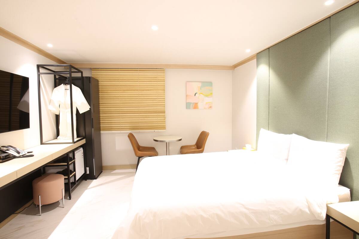 Ein Hotelzimmer mit einem Bett, einem Schreibtisch mit Telefon, einem Sessel, einem kleinen Tisch und einem Wandbild.