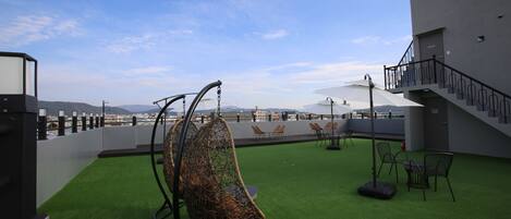 A rooftop terrace with artificial grass, a hanging chair, outdoor seating, and a staircase.