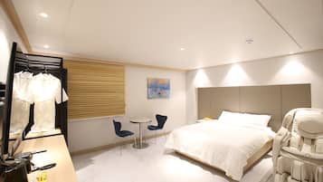 A modern hotel room with a bed, massage chair, two chairs, a small table, and a mirror.