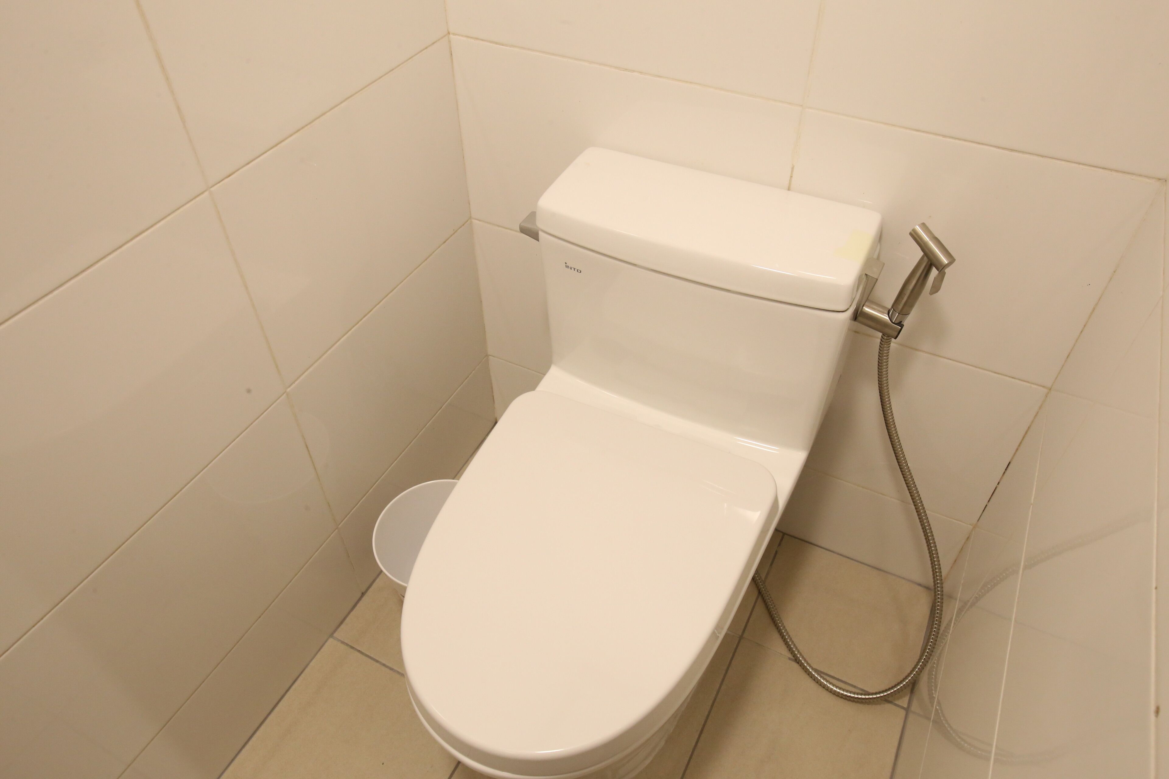 A white toilet with a shower attachment in a bathroom with white tiled walls.