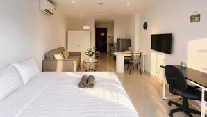 Quarto de hotel com cama, mesa de trabalho, cadeira, televisão e cozinha compacta.