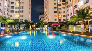Piscina cercada por edifícios altos com varandas, palmeiras e letreiros iluminados.
