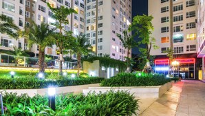 Um pátio urbano bem iluminado com edifícios modernos, vegetação exuberante e uma entrada luminosa.