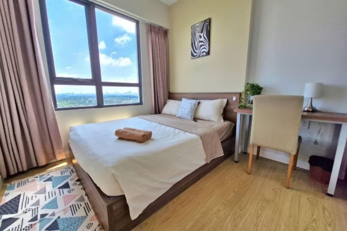 A hotel room with a bed, a desk, a chair, a window with curtains, and a wall-mounted artwork.