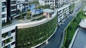 Un edificio residencial moderno con varios pisos, balcones y un área ajardinada con piscina.