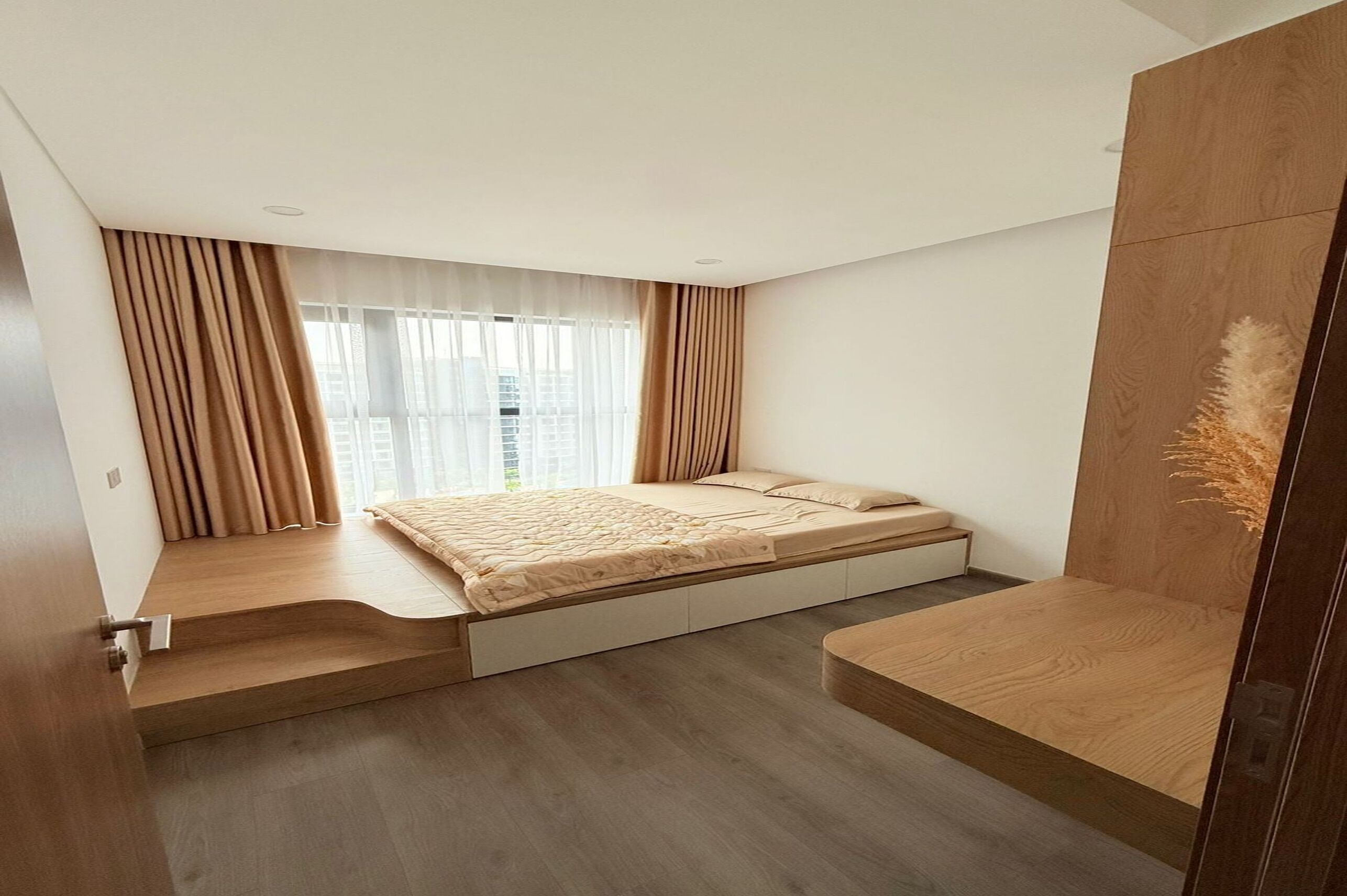 A modern bedroom with a built-in bed, a small bedside table, and a view of the city through sheer curtains.