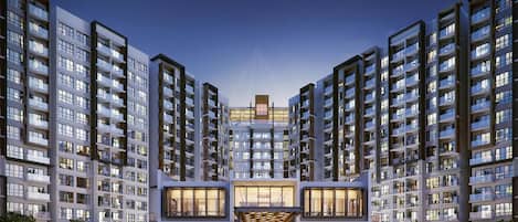 A modern apartment complex with multiple high-rise buildings, a central entrance with glass doors, and a well-maintained landscaped area.