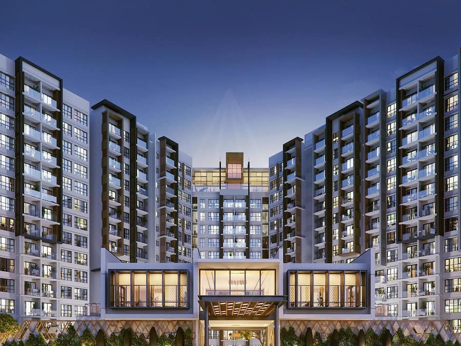 Un moderno complejo de apartamentos con varios edificios de gran altura, una entrada central con puertas de cristal y una zona ajardinada bien cuidada.