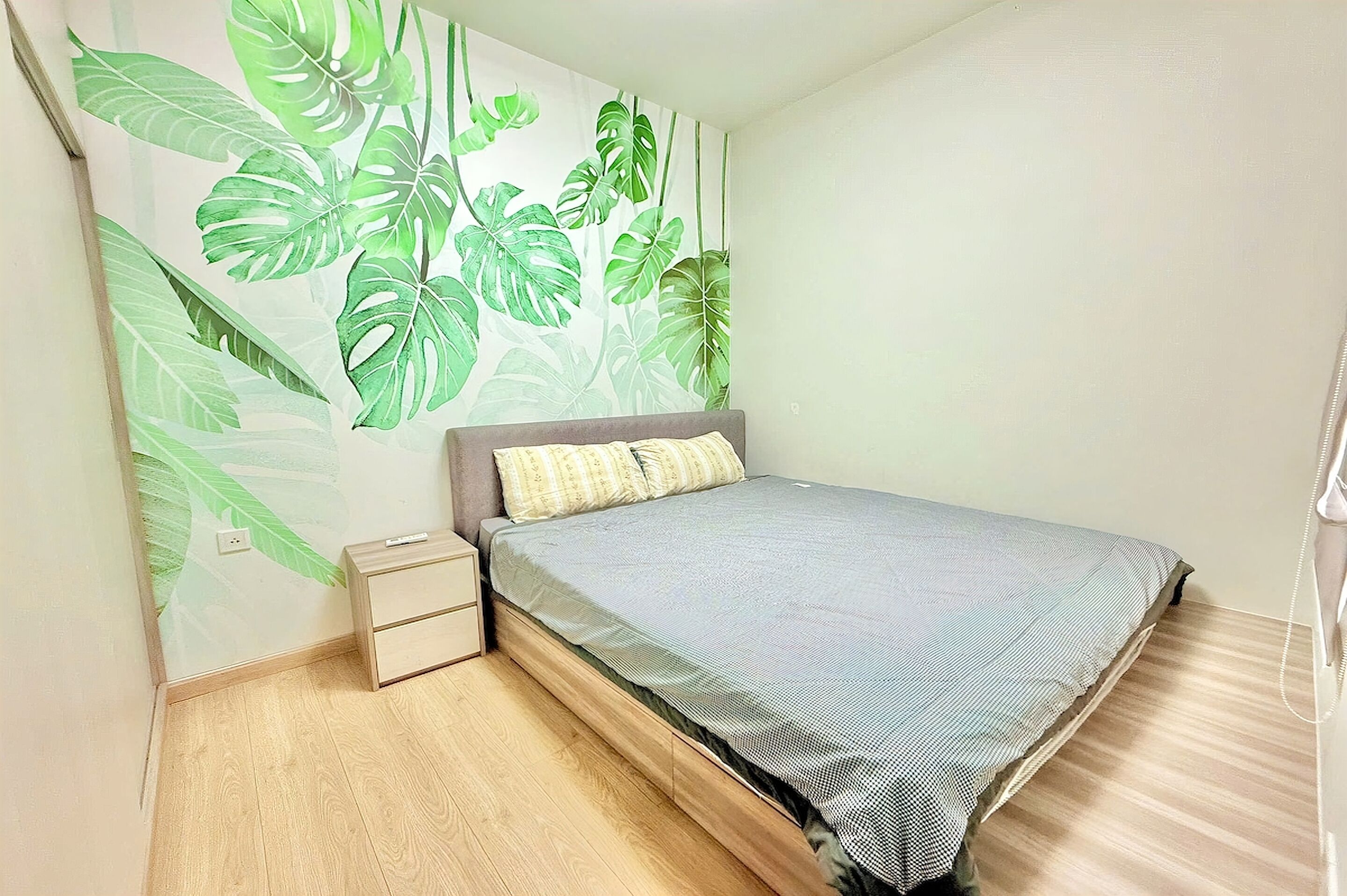 Ein Schlafzimmer mit einem Bett, einem Nachttisch, einem fest montierten Telefon und einer Wand mit einem grünen Blattmuster.