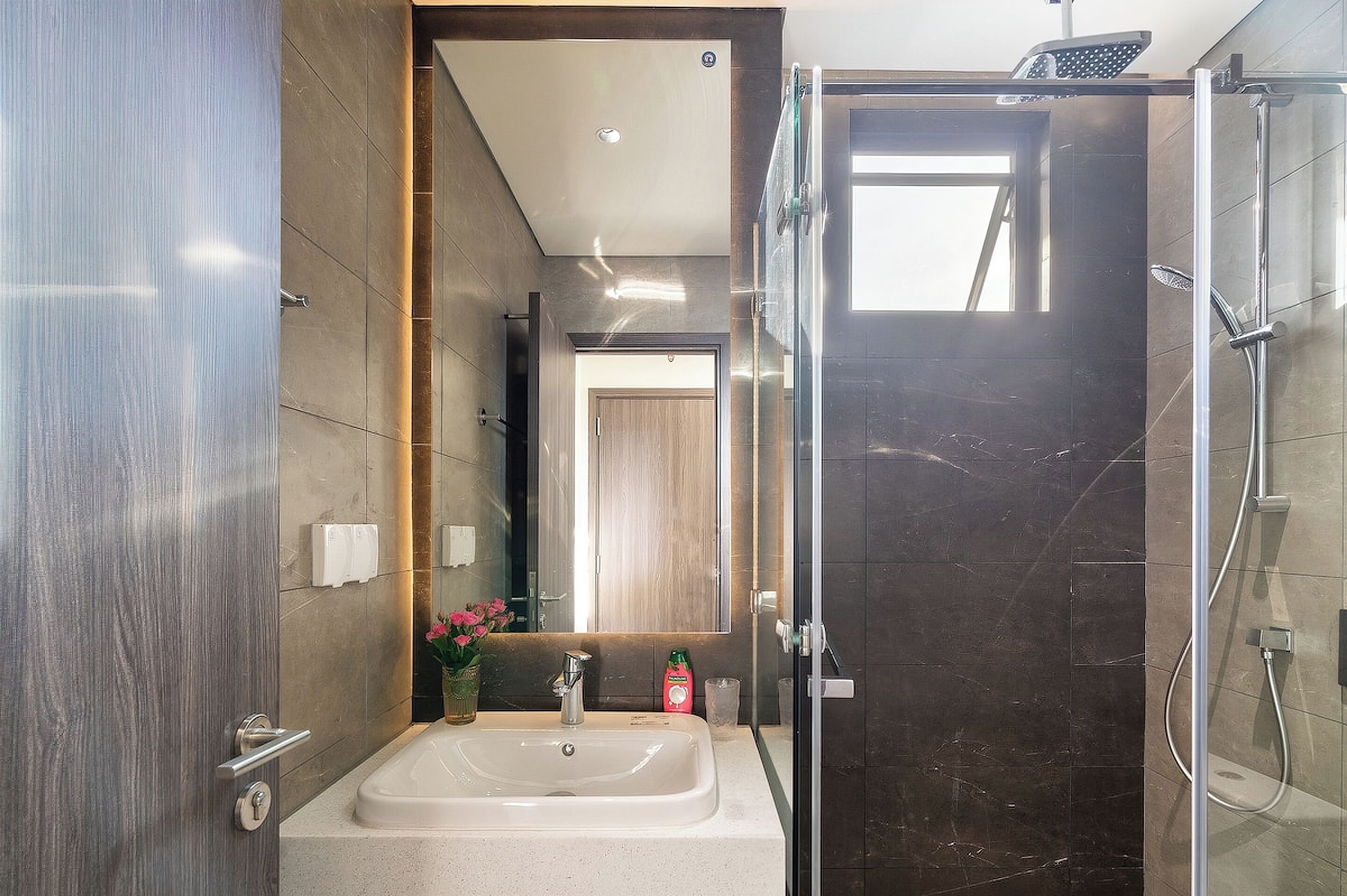 Un baño moderno con lavamanos, espejo, ducha y una puerta que da a otra habitación.