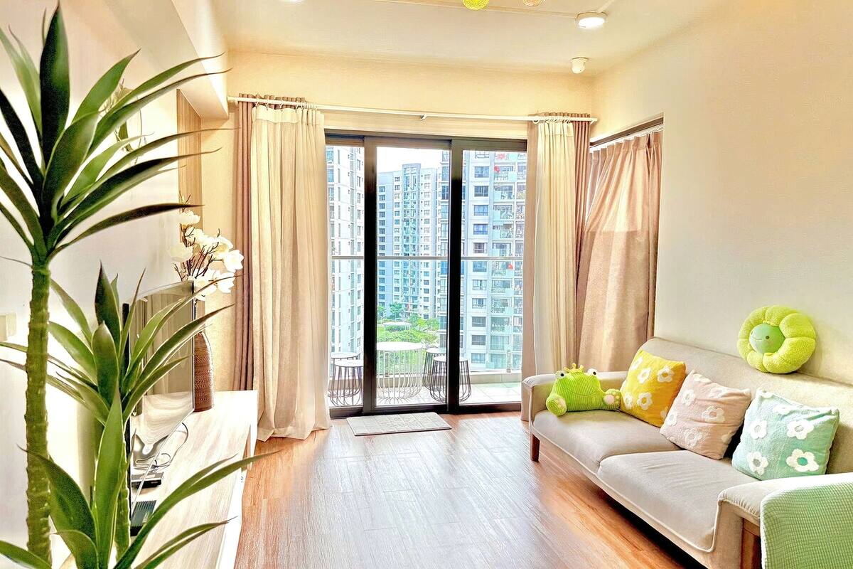 A modern living room with a sofa, a plant, and a view of high-rise buildings through the glass door.