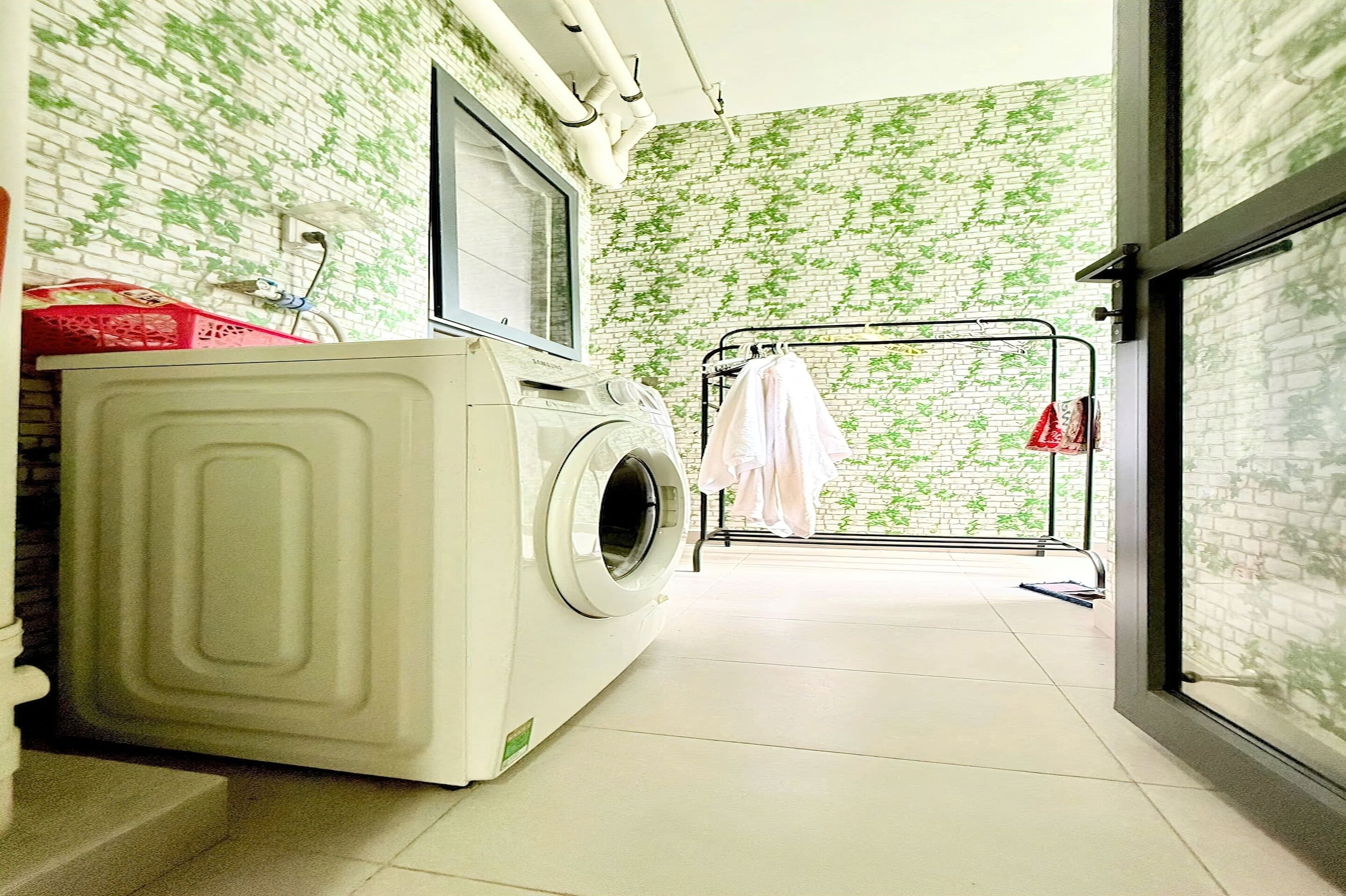 A laundry room with a washing machine, a drying rack, and a brick-patterned wall.