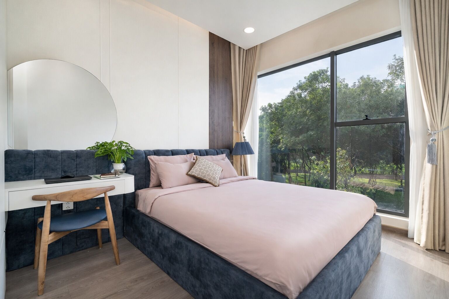 A bedroom with a bed, a desk, a chair, a mirror, and a window with a view of greenery.