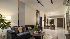 Ein modernes Wohnzimmer mit einem dunklen Sofa, einem runden Couchtisch und einem Essbereich im Hintergrund.