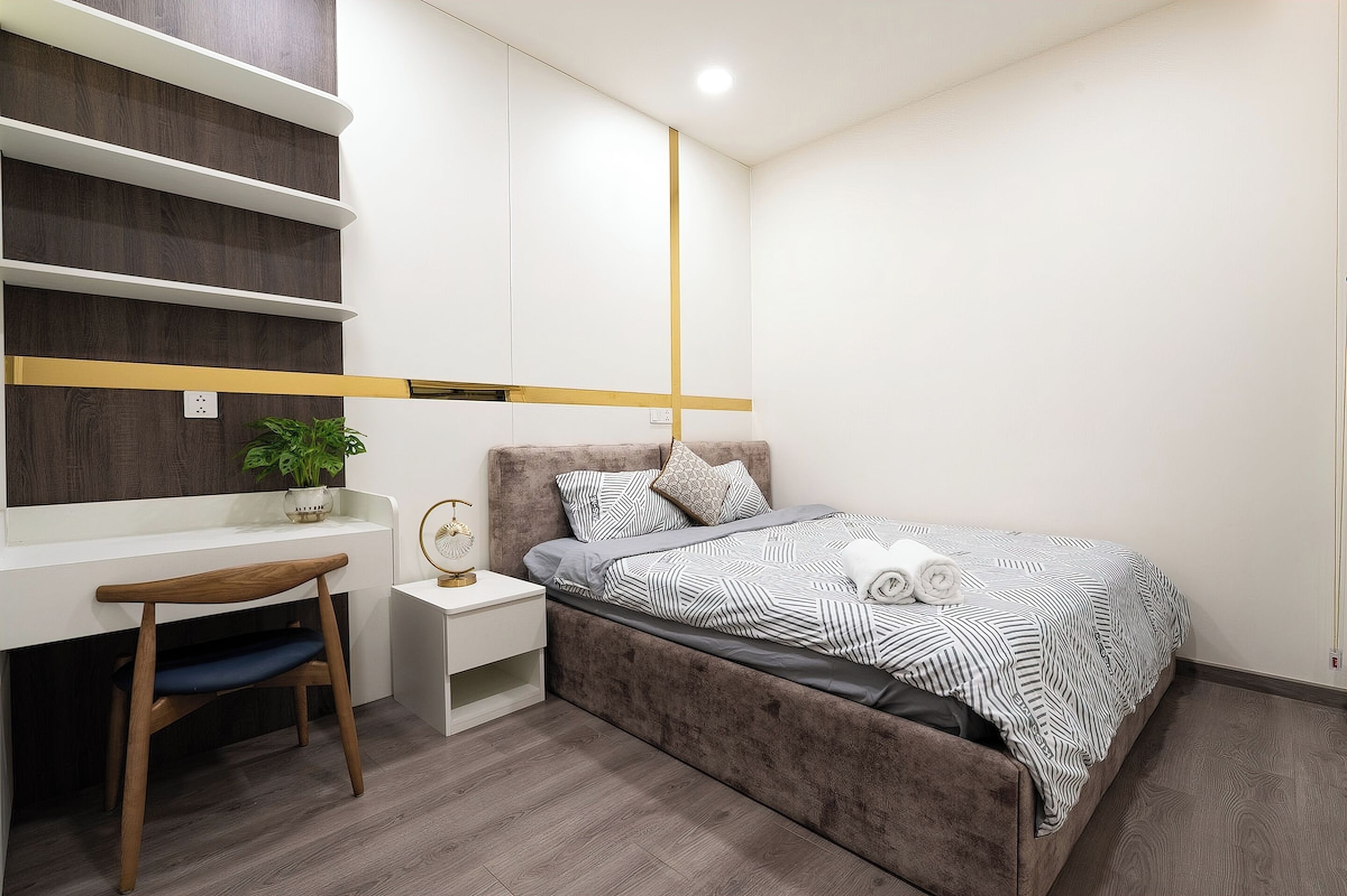 A bedroom with a bed, bedside table, chair, and a desk with a plant.