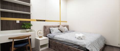 A bedroom with a bed, bedside table, chair, and a desk with a plant.