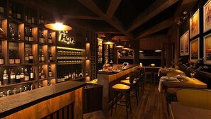 A bar area with wooden shelves stocked with bottles, a counter with stools, and framed artwork on the walls. - Diamond Island - Mekong Retreat Apartment (Ho Chi Minh City)