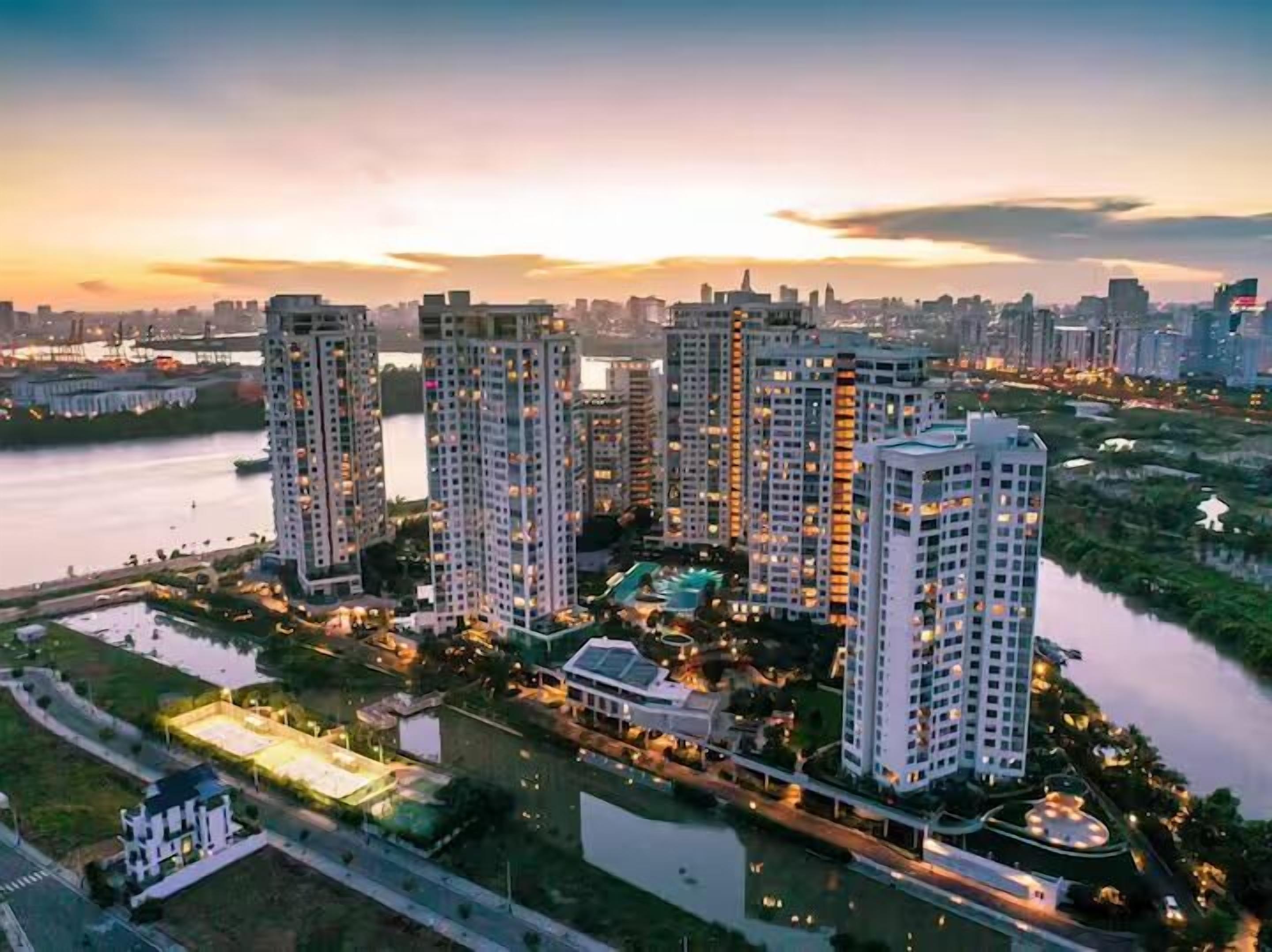 A high-rise residential complex with multiple buildings, a river, and a well-lit park area.
