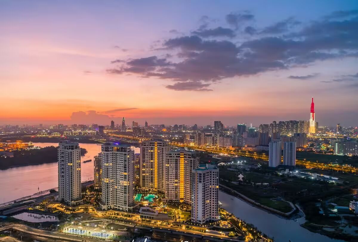 A high-rise residential building complex with multiple towers, a river, and a city skyline in the background.