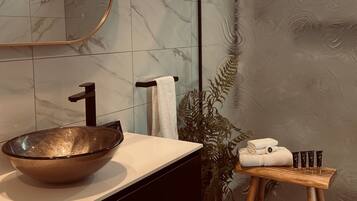 A modern bathroom with a large mirror, a glass bowl sink, and a wooden stool with toiletries.