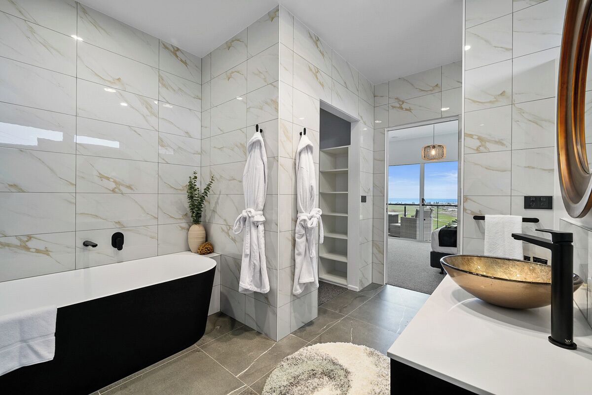 Un baño moderno con una bañera grande, un lavamanos con un lavabo dorado y dos toallas blancas colgadas de ganchos.