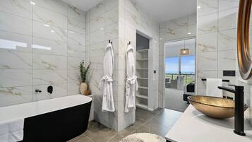 Un baño moderno con una bañera grande, un lavamanos con un lavabo dorado y dos toallas blancas colgadas de ganchos.