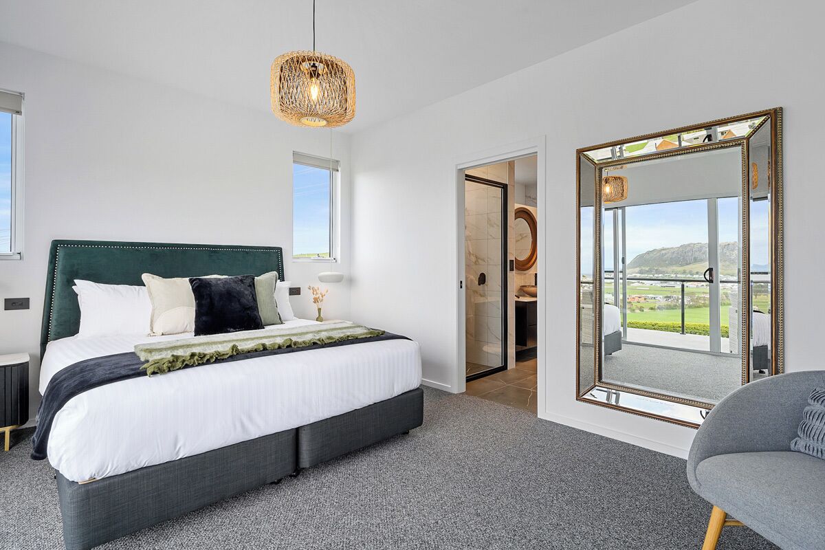 A bedroom with a large bed, a mirror, and a view of the outdoors.