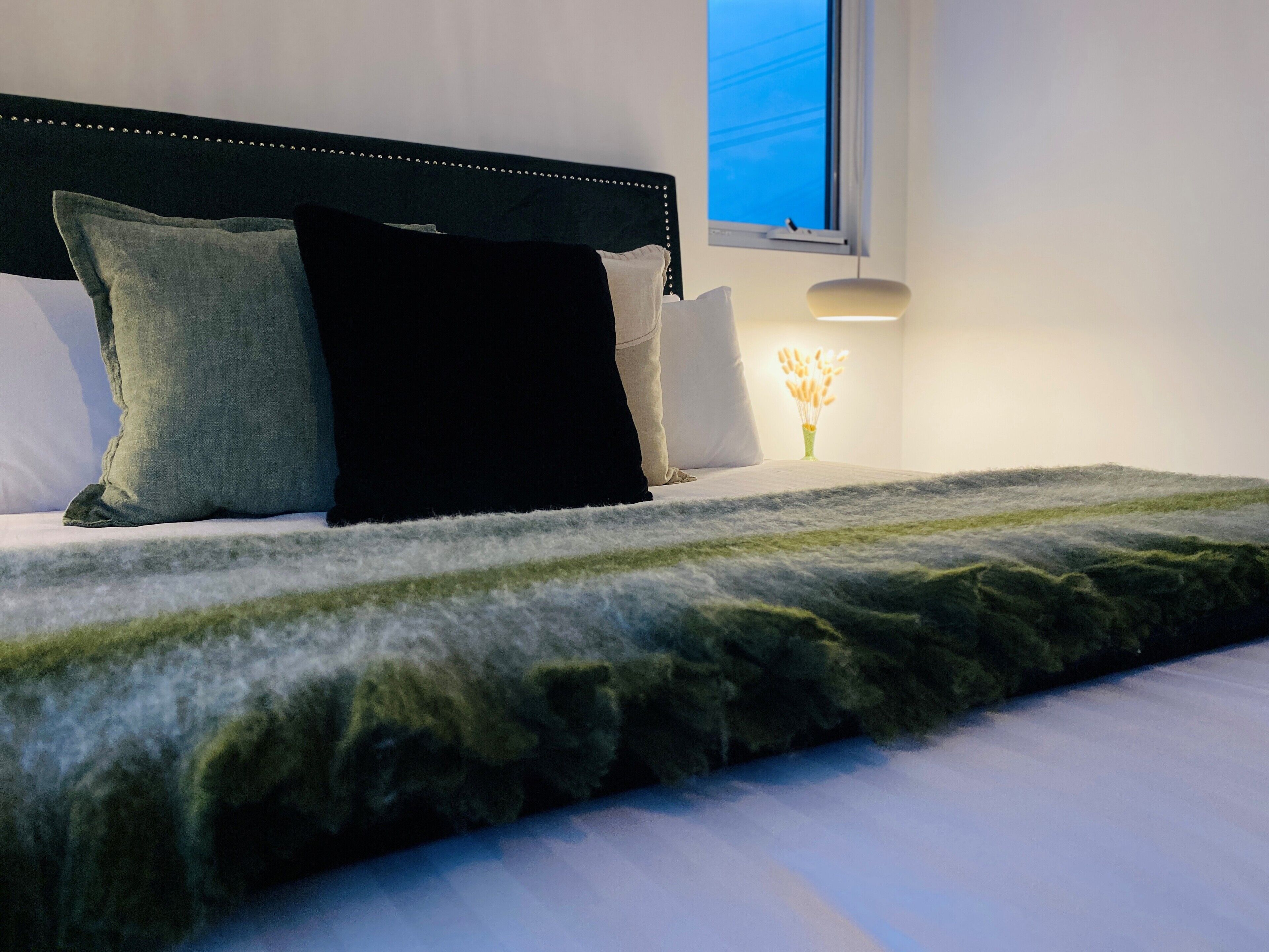 A neatly made bed with a dark headboard, white pillows, and a green throw blanket.