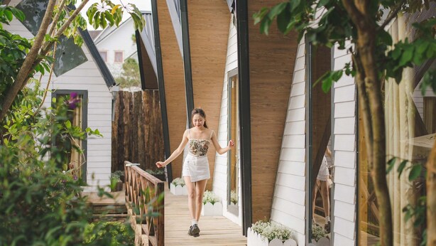 A person walking on a wooden deck with a modern house in the background. - Windy Hill Homestay (Xuan Truong - Da Lat)