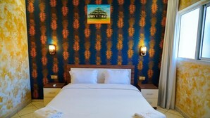 A hotel room with a large bed, two bedside tables, a nightstand, a painting on the wall, and a window with curtains. - Apartments next to the beach  (Agadir)
