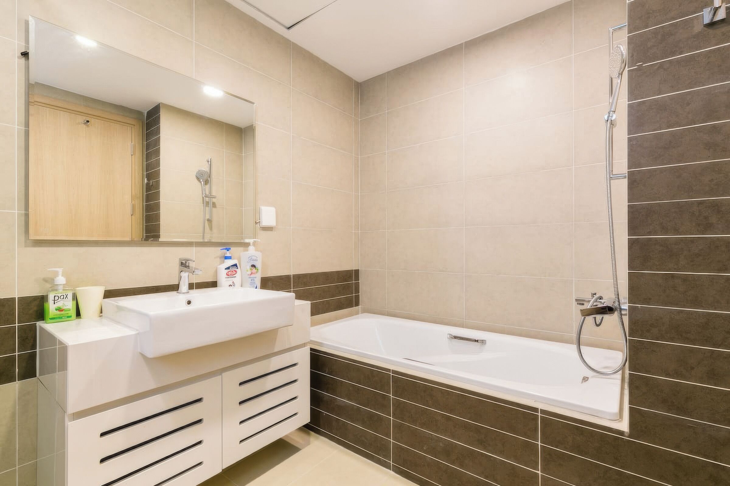A modern bathroom with a white sink, mirror, and a bathtub with a showerhead.