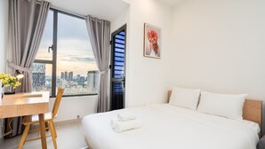 Una habitación de hotel moderna con una cama grande, un escritorio con silla y vistas a la ciudad a través de un amplio ventanal.