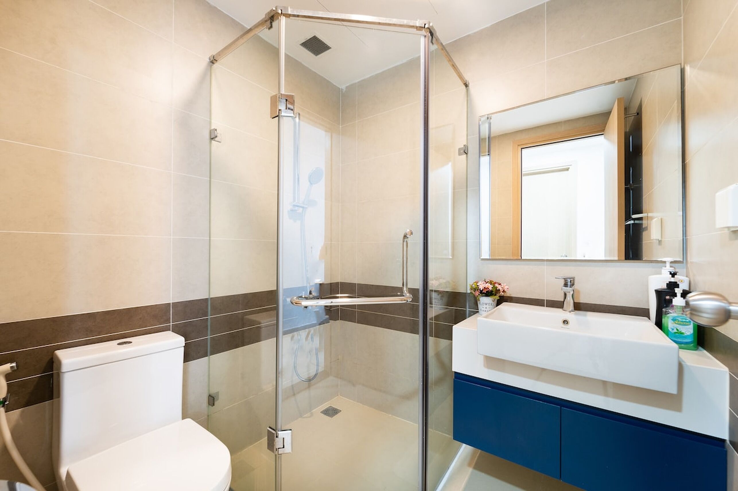 Une salle de bain moderne avec une douche à l’italienne en verre, un lavabo blanc avec un meuble bleu, et un grand miroir au-dessus du lavabo.