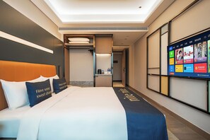 Een hotelkamer met een bed, een televisie waarop verschillende apps worden weergegeven, en een klein keukenhoekje.
