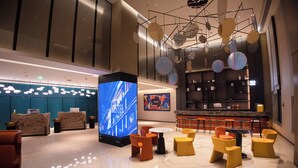 Um hall moderno com uma grande tela digital, diversas áreas de estar e um bar.