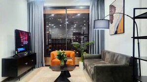 A modern living room with a flat-screen TV, a sofa, an orange armchair, and a coffee table. - GEM Residence - The Manor Central (Ho Chi Minh City)
