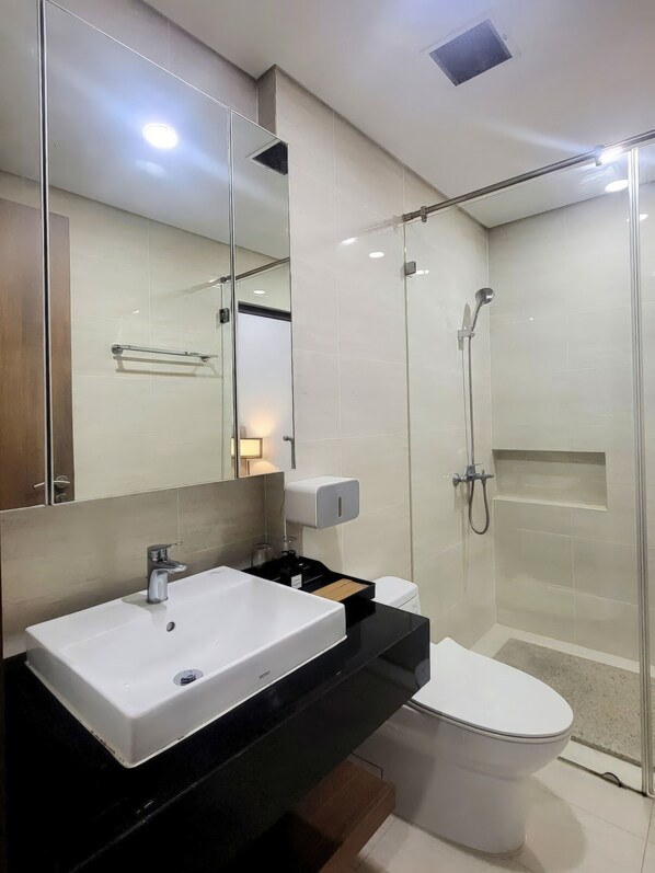 A modern bathroom with a white sink, a toilet, a glass shower enclosure, and a mirror. - The Manor By Emily In Town (Ho Chi Minh City)