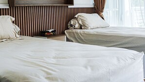 A hotel room with two beds, a wooden headboard, a nightstand, and a window with curtains. - GRIYA GRACHIKA by DOORKOST (Sewon)
