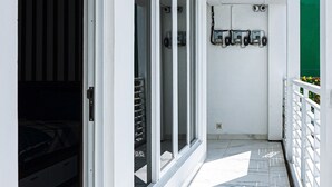 A narrow corridor with a bed on the left, a sliding glass door, and a white railing on the right. - GRIYA GRACHIKA by DOORKOST (Sewon)
