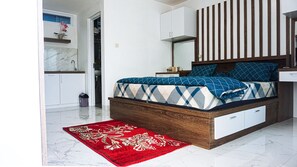 A bedroom with a bed, a nightstand, a dresser, and a red patterned rug. - GRIYA GRACHIKA by DOORKOST (Sewon)