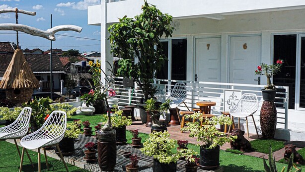 A modern two-story building with a balcony, potted plants, and outdoor seating. - GRIYA GRACHIKA by DOORKOST (Sewon)