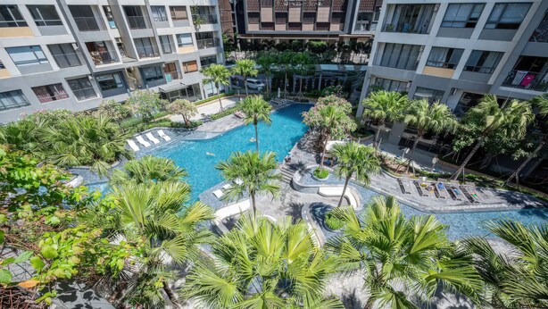 Un hotel de varios pisos con una piscina central rodeada de palmeras y zonas de descanso.