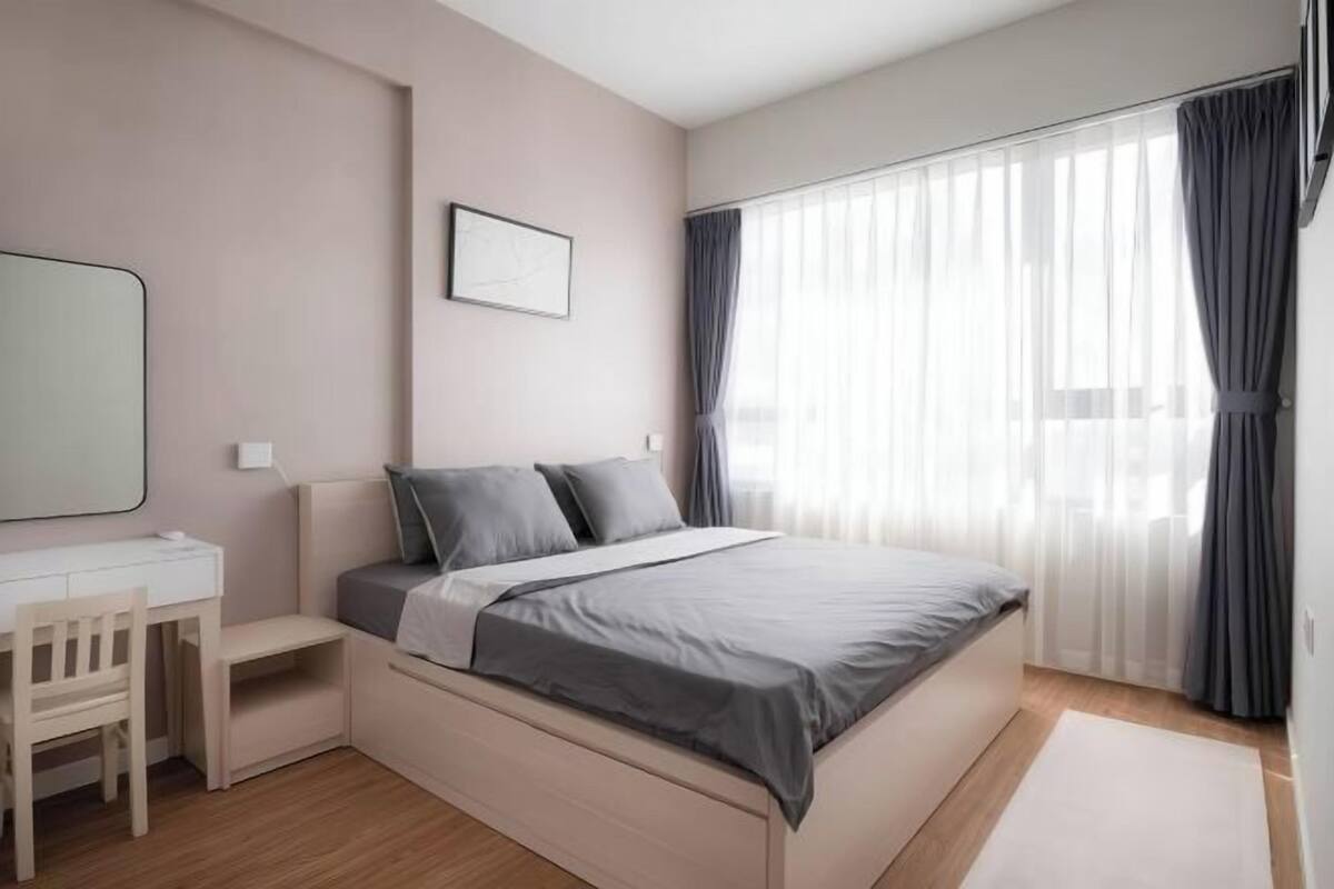 Une chambre à coucher comprenant un lit, un bureau, une chaise, une fenêtre avec des rideaux et un tableau encadré accroché au mur.