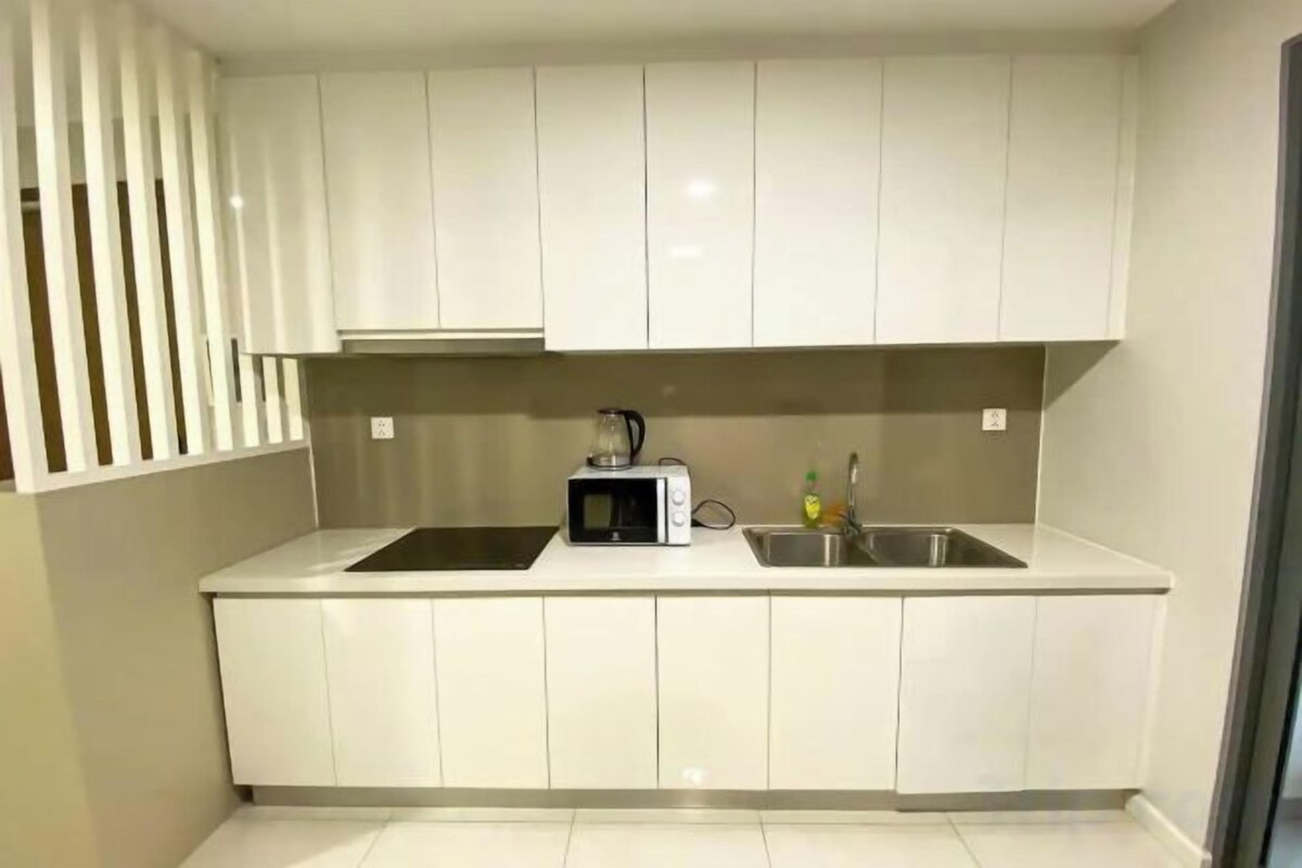 A modern kitchen with white cabinets, a black induction cooktop, a microwave, and a stainless steel sink.