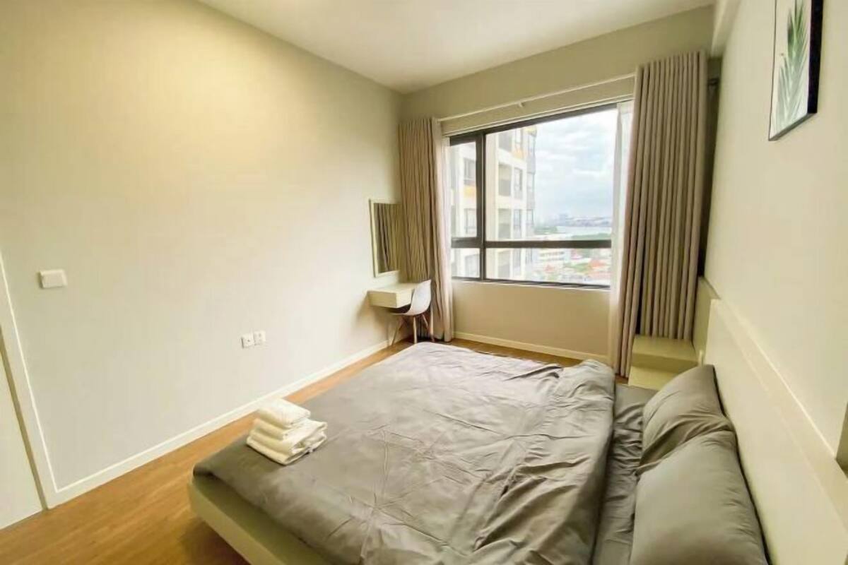Une chambre d’hôtel avec un lit, un bureau, une chaise, une fenêtre avec des rideaux et une vue sur des immeubles.