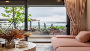 A modern room with a large window, a sofa, a table with a candle, and a vase of dried flowers. - Lumiere Riverside - Luxury Condo District 2 (Ho Chi Minh City)