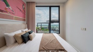 A modern hotel room with a large bed, a view of the city through a large window, and a tennis-themed mural on the wall. - Lumiere Riverside - Luxury Condo District 2 (Ho Chi Minh City)