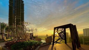 A rooftop terrace with a wooden deck, a small garden area with plants, and a view of a tall building in the background. - Lumiere Riverside - Luxury Condo District 2 (Ho Chi Minh City)