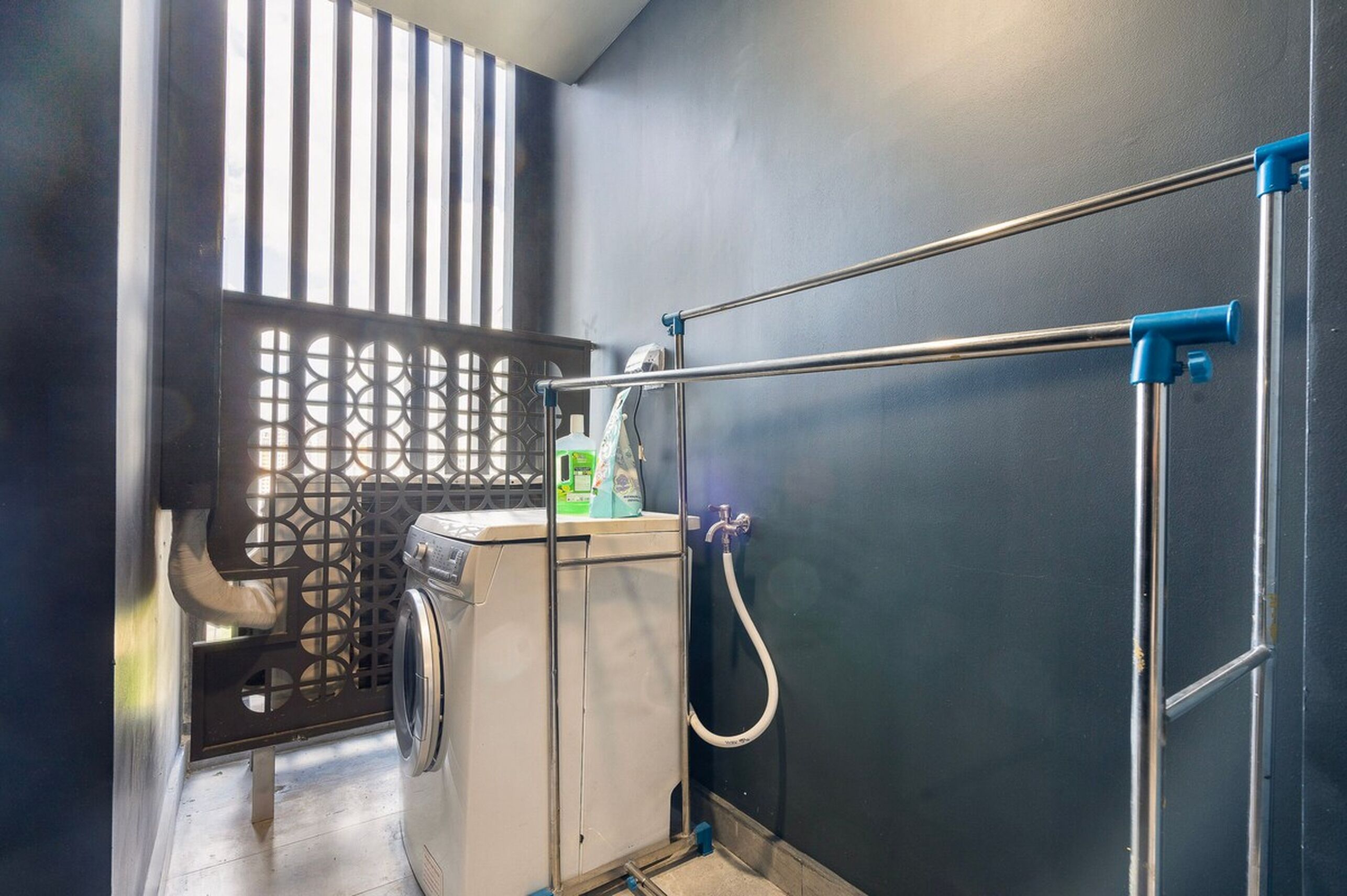 Un espace dédié à la lessive, équipé d’un lave-linge, d’un étendoir et d’un tuyau d’eau.