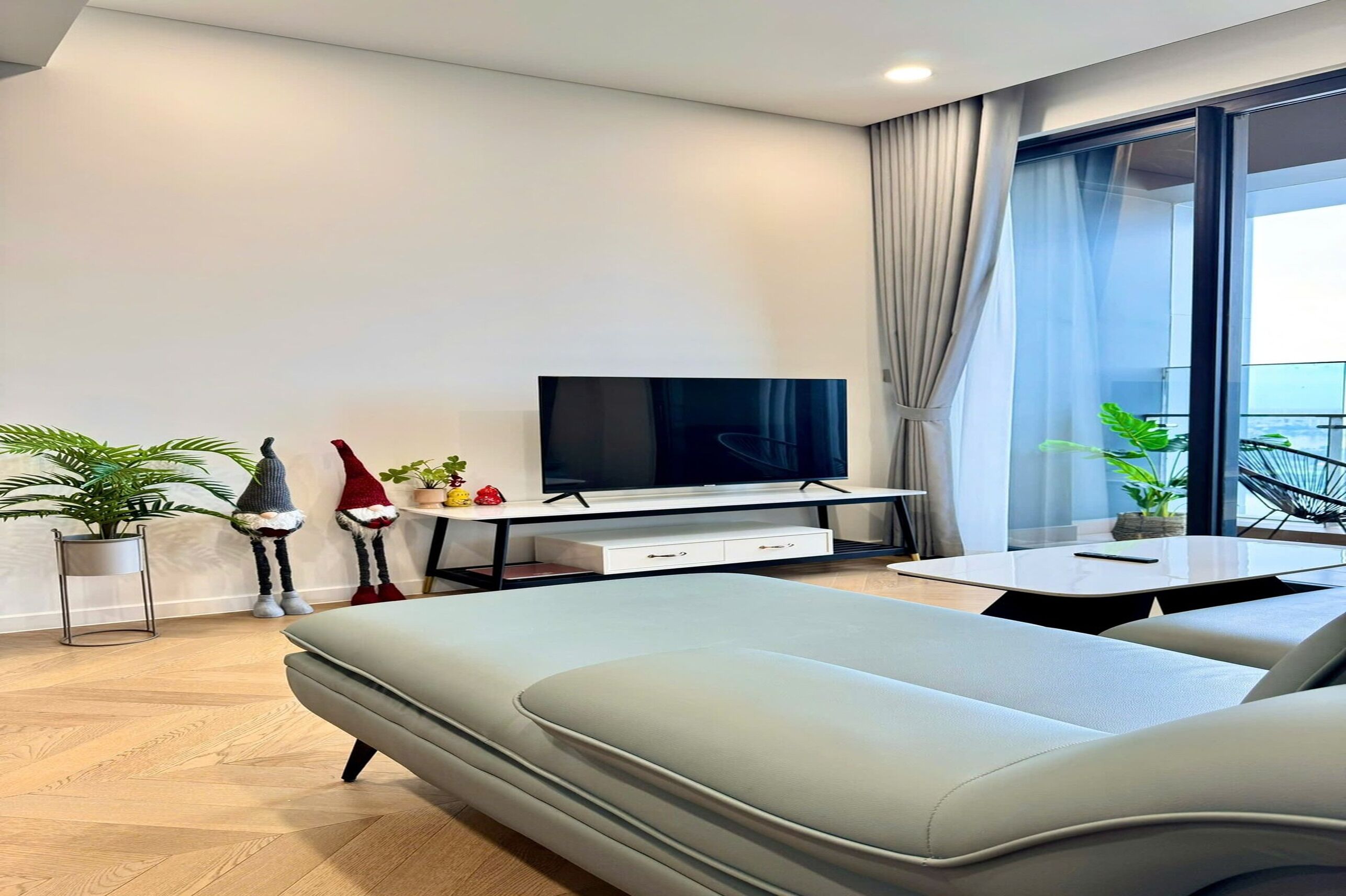 A modern living room with a sofa, a flat-screen TV, a dining table, and potted plants.